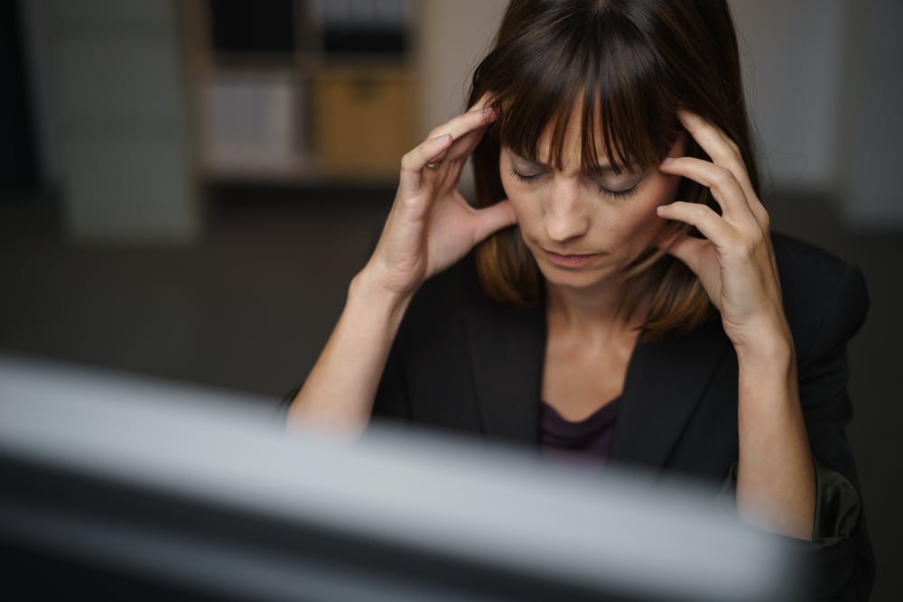 Businesswoman suffering from a headache or migraine holding her hands to her throbbing temples as she works late in the office to a deadline